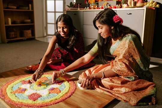 Asian young adult women decorating traditional festival pattern on floor celebrating holiday culture. Ideal for cultural diversity campaigns, festive promotions, marketing projects
