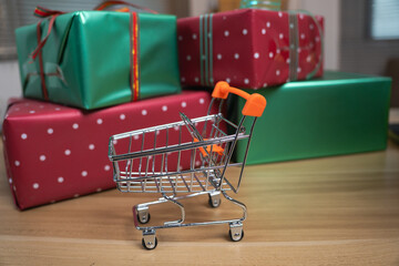 Miniature shopping cart next to stacked Christmas gift boxes for holiday sale concept © Oil And Den