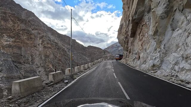POV video as a vehicle drives on a mountain curvy  road alongside a massive smooth rock overhang with concrete bollards Spiti Valley Himachal Pradesh India | Himalayan road trip GoPro dashcam 4K