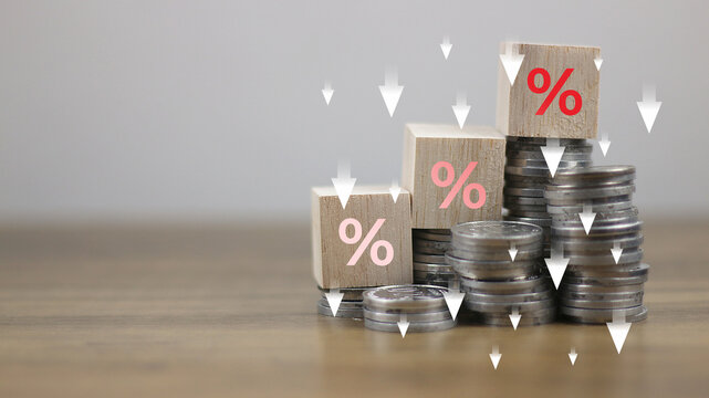 Show percentage icon on wooden blocks on coin stacks with down arrows, concept of interest rate adjustment, special offer, inflation, returns on investments, discount, tax, and financial management