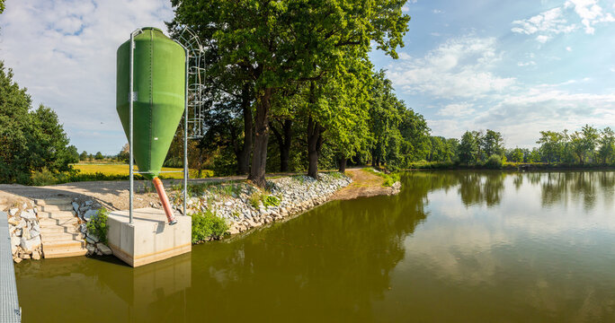 Green fish feed bulk silo on a tranquil pond dam