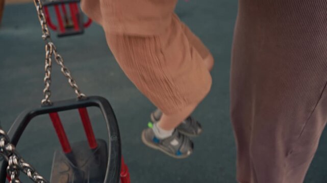 Young child in brown outfit explores and interacts with playground equipment guided by adult. sequence captures moments of boy hands on chains feet near swings and details of his clothing