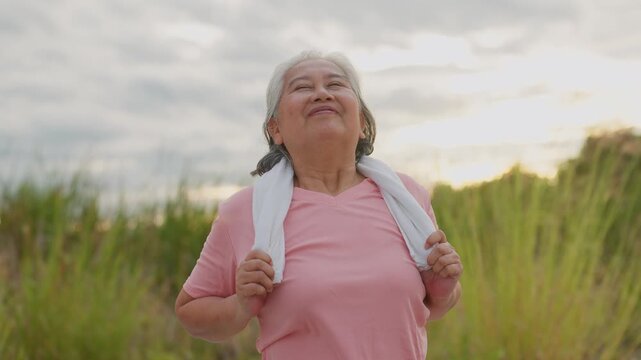 Sunset warms the grassy field behind her. She smiles, joyful after her run. Towel rests around her shoulders. Her pink top shows her effort