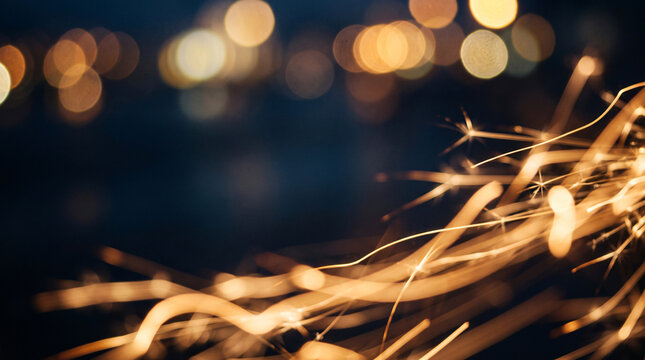 Bright burning sparkler trails against a dark night sky with warm bokeh lights