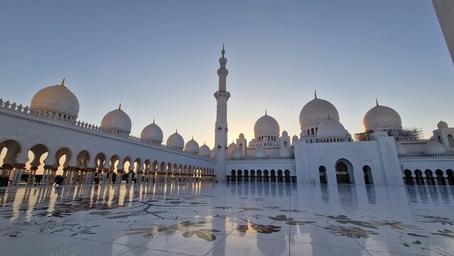 White mosque courtyard with domes minaret arches and reflections