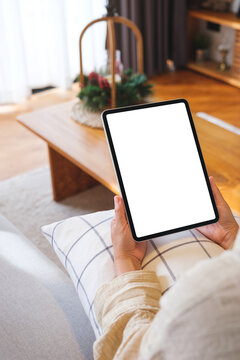 Vertical mockup image of a woman holding tablet with blank desktop white screen at home