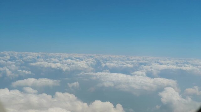 Airplane wing above sunlit clouds seen through window