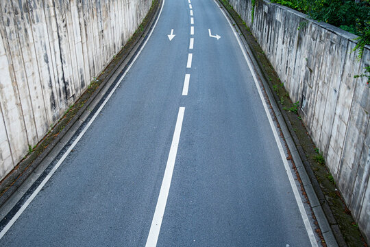 Empty road curves between concrete walls in Lyon France with directional arrows and lane markings creating a clean urban transport corridor