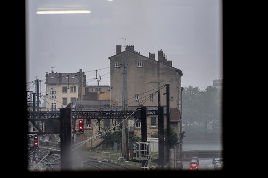 Rainy railway scene in Lyon France shows tracks signals and older urban buildings through wet weather creating a muted city transport atmosphere