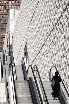 Pedestrian rides an escalator beside a textured building facade in Lyon France creating a strong urban geometry of steps lines and architecture