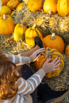 Woman Holding Pumpkin at Autumn Harvest. Woman holding a pumpkin among hay and colorful pumpkins in an autumn harvest setting.