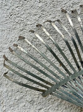 Metal Leaf Rake Tines Against Textured Wall Background