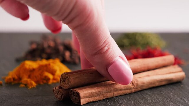 Hand picking cinnamon stick from table with assorted spice piles. Aromatic seasonings and oriental cuisine concept.