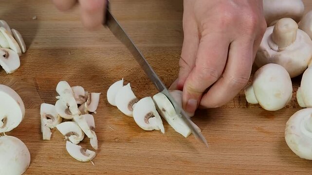 Raw mushrooms champignons are cut into slices with a knife on a wooden cutting Board. Close up.