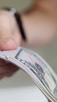 Close-up of male hands counting a thick stack of dollar bills. Concept of finance, wealth, business success, payment, or corruption. Vertical video.
