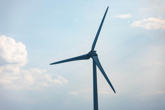 Single wind turbine set against a clear blue sky with clouds, symbolizing renewable energy, sustainability, and clean power generation.
