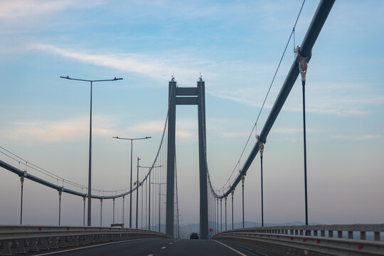 Wide view of an empty suspension bridge under a blue evening sky, emphasizing symmetry, modern engineering, and tranquil urban transportation.