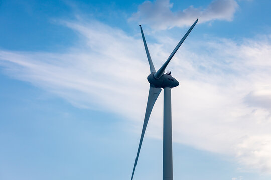 Single wind turbine with large blades set against a blue sky with soft clouds, symbolizing clean energy and sustainability.