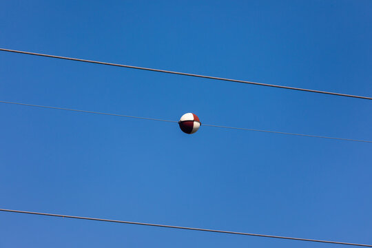 Red and white marker ball on overhead power lines against clear blue sky, symbolizing safety, energy, and communication.