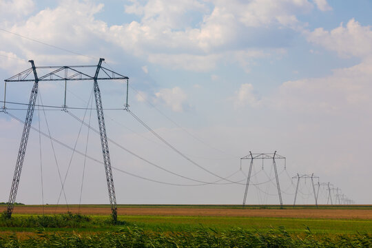 High voltage power lines stretch across an open rural landscape under a bright, partly cloudy sky, symbolizing energy, infrastructure, and connectivity.
