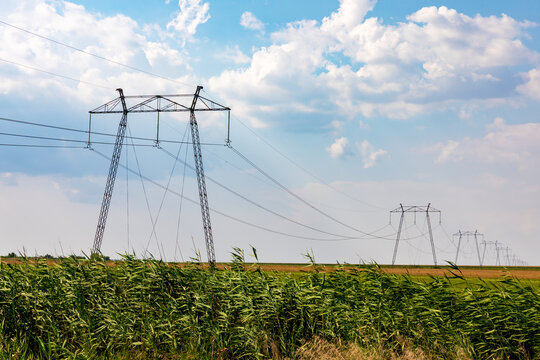High-voltage power lines stretch across open rural fields under a bright, partly cloudy sky, symbolizing energy and infrastructure.