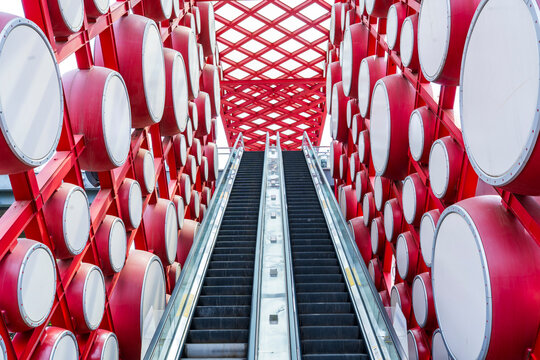 An outdoor escalator. On both sides are red drums.