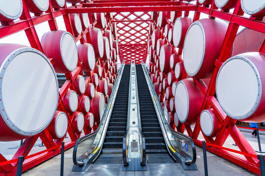 An outdoor escalator. On both sides are red drums.