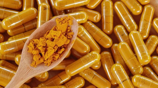 Turmeric powder in a wooden bowl and spoon, and there are turmeric capsules.