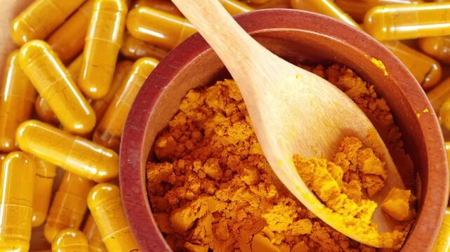 Turmeric powder in a wooden bowl and spoon, and there are turmeric capsules.