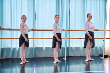 Adult female ballerinas practice barre in bright ballet studio with blue light © TRAVELARIUM