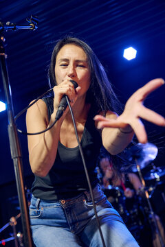 Young woman singing during band sound check under blue stage lights