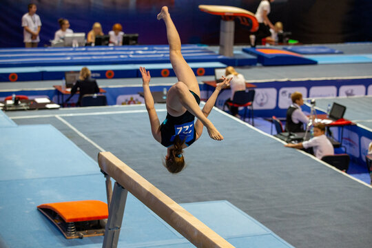 Female gymnast performing acrobatic flip above balance beam