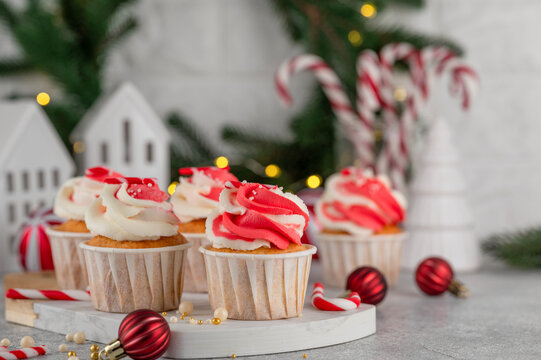 Festive Christmas vanilla cupcakes with red and white swirled buttercream frosting and candy cane on top in the gray background. Christmas dessert on the board. Copy space.