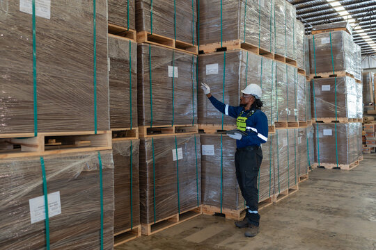 Export shipment packaging inspection: a man holds a tablet and points toward wrapped pallets stacked in the warehouse.