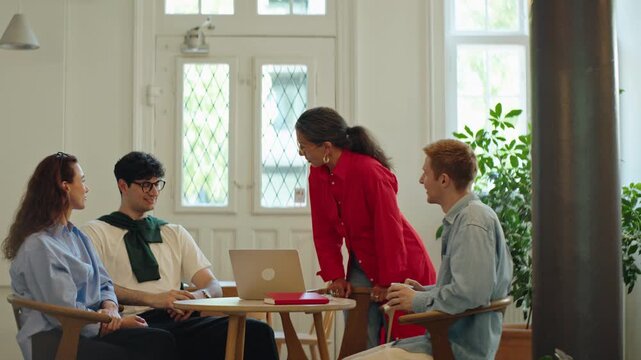 Coworker joins as team celebrates progress during a business meeting in a cafe office, with collaboration, discussion, and startup teamwork around a table in a flexible workplace.
