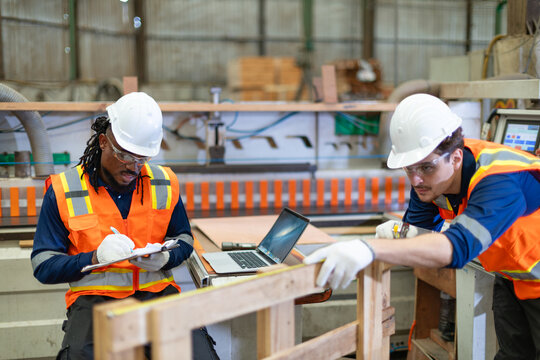 During plywood woodworking, a carpenter measures a frame while his colleague records dimensions on a clipboard in the wood workshop.