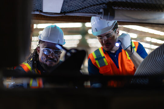 Checking machine maintenance needs, a technician and his colleague use a flashlight to inspect internal components of an open moulder.