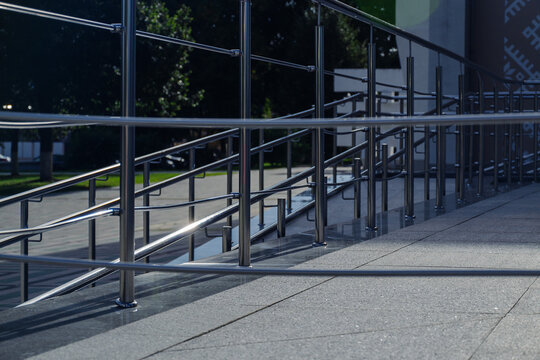 Shiny stainless steel handrails and protective barriers mounted on stone tile ramp structure of public building