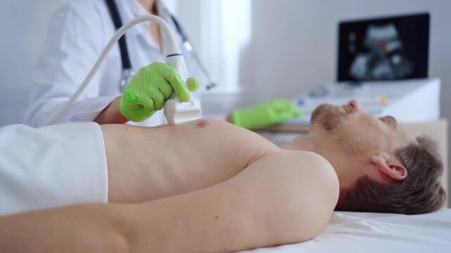 Doctor woman with green medical gloves performing an ultrasound scan of male patient breast lying down in clinic procedure cabinet. Cardiology diagnosis and medicine service concept