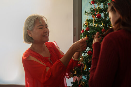 Senior Asian mother decorating Christmas tree with adult daughter at home
