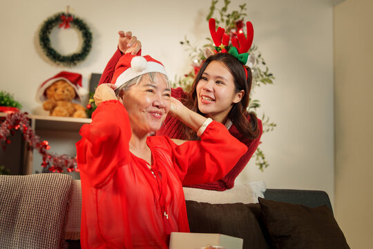 Asian daughter helping senior mother put on Santa hat for Christmas