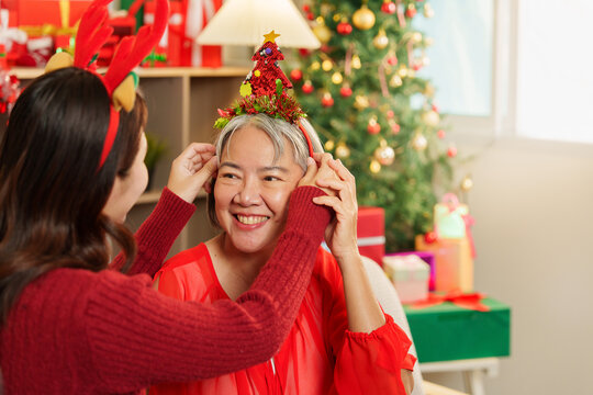Asian daughter adjusting Christmas tree headband on senior mother close up