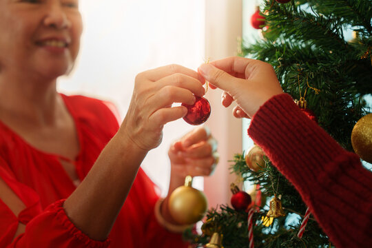 Close up of hands decorating Christmas tree with red ornament