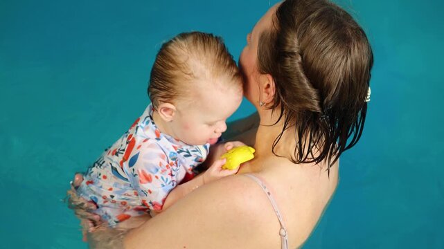 Mother holding baby wearing swimsuit in indoor swimming pool water