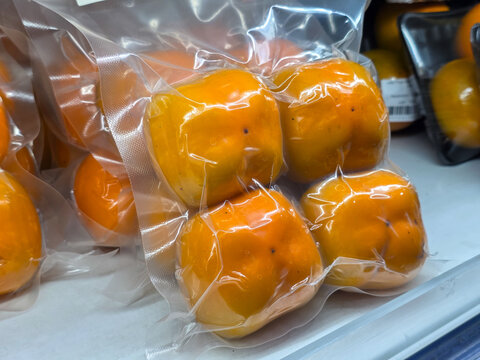 Vacuum packed orange fruit arranged in clear plastic bag, showing fresh produce, glossy skin, and retail market packaging with warm color and natural texture