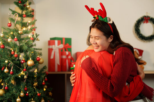 Asian daughter hugging senior mother near Christmas tree at home for holiday togetherness