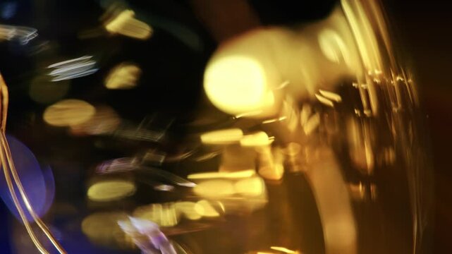 Macro shot of warm golden light reflections and dynamic bokeh streaks moving across curved glass against a dark background.