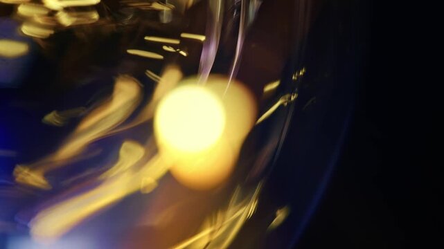 Macro shot of swirling golden light streaks and curved glass refractions creating dynamic bokeh against a dark background.