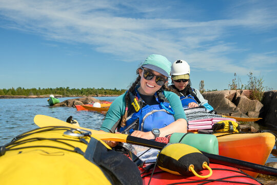 Smiling kayaker and paddling partner rafted up among colorful sea kayaks loaded with gear under blue sky with copy space, Georgian Bay, Ontario