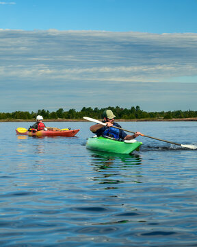 Vertical view of a man paddling a green sea kayak with a splashing stroke as a companion follows, sky copy space above, Georgian Bay, Ontario